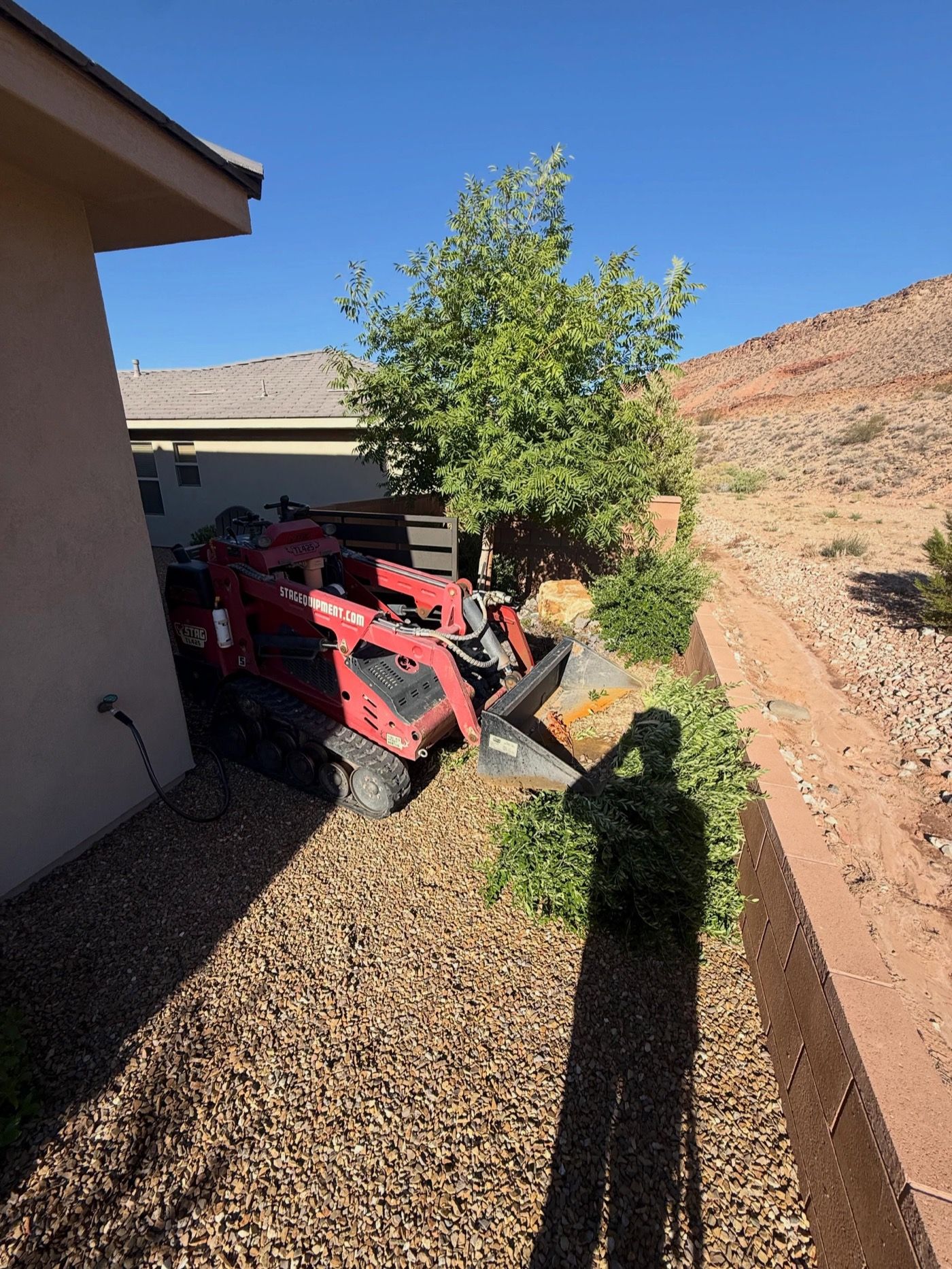During: a compact track loader in the side yard, mid-job